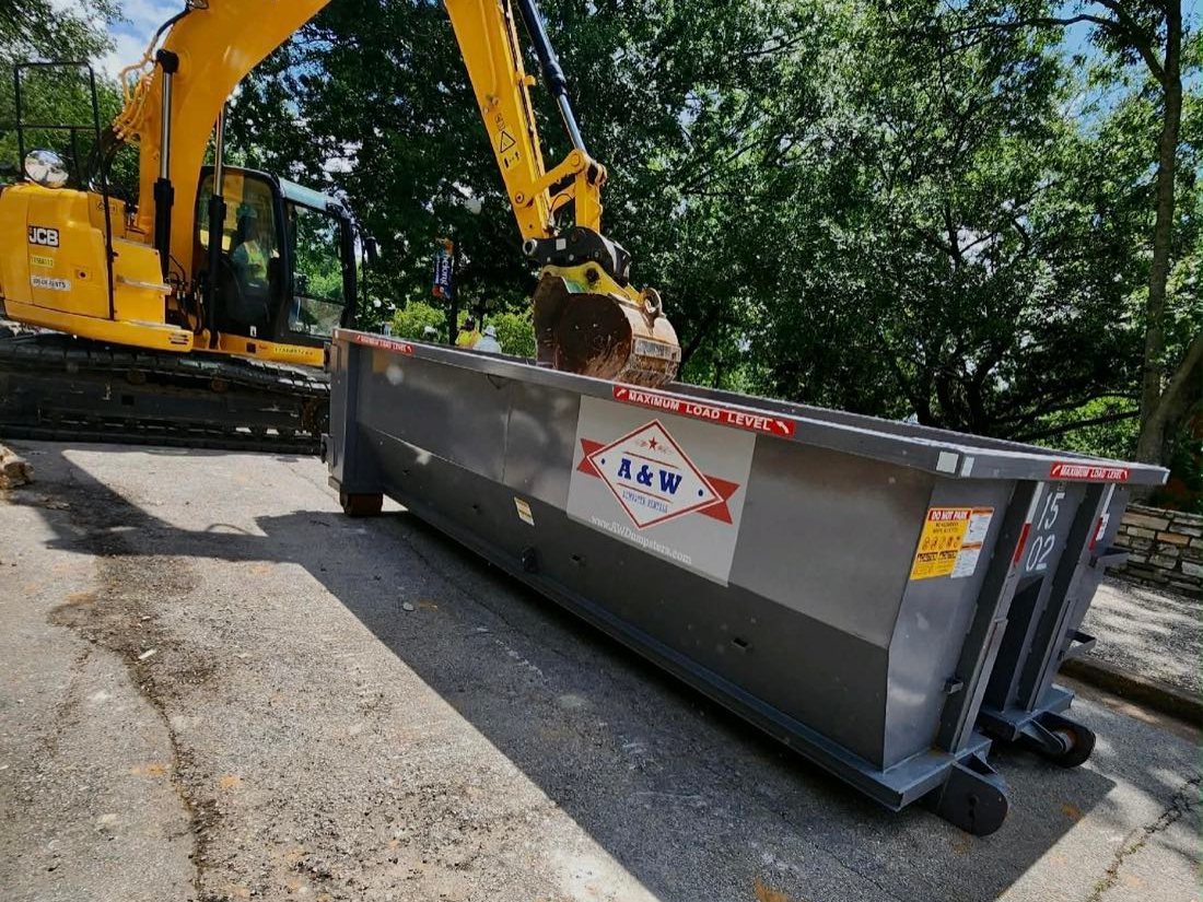 Excavator loading an A&W roll-off dumpster on a demolition job