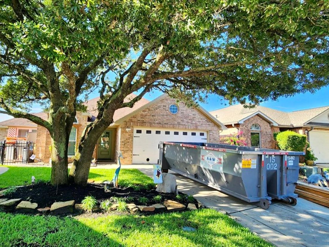 A&W roll-off dumpster on a residential driveway under mature oaks