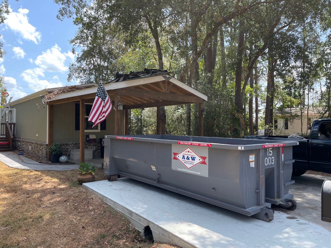 A&W branded 15 yard dumpster beside a home flying the American flag
